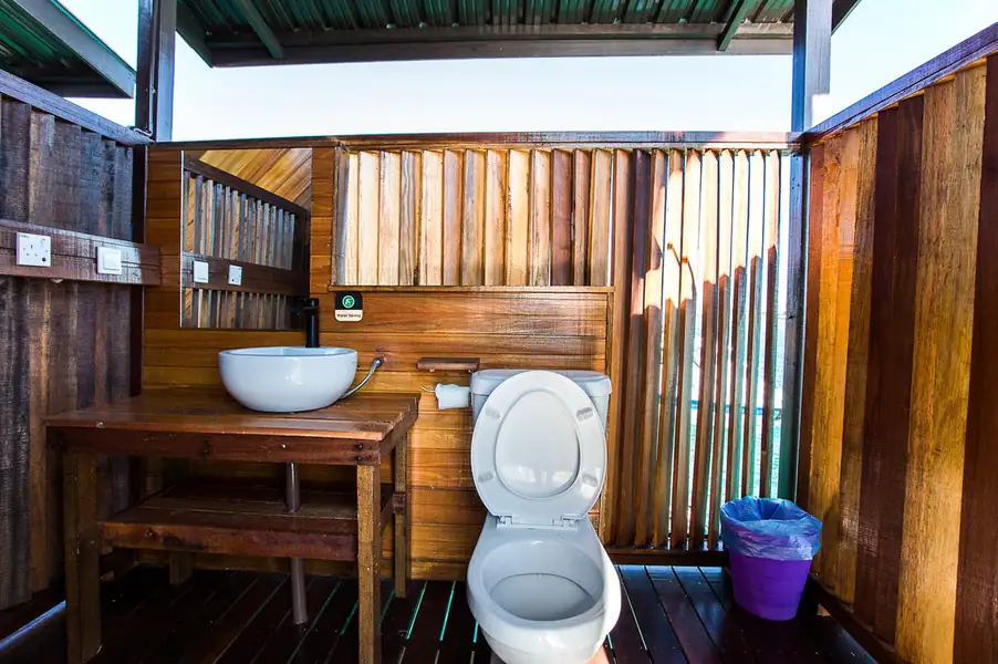 A clean and brightly lit bathroom featuring a modern vanity with an illuminated round mirror, a classic white toilet, tiled walls, a frosted window, and a corner electric shower at Sea Coral Resort.