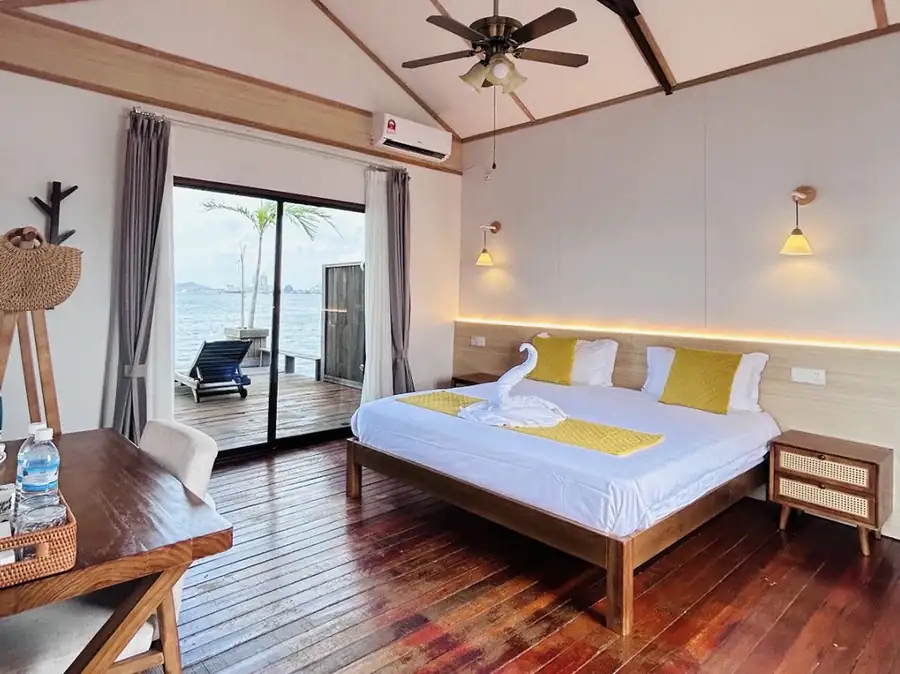 A tranquil bedroom at Sea Coral Resort in the Celebes Sea where a large bed faces direct access to the private balcony via glass doors, dark polished timber boards, and a/c.