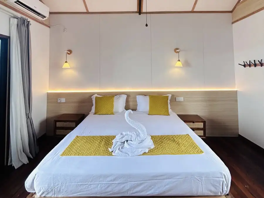 A stylish bedroom at Sea Coral Resort in the Celebes Sea featuring a large bed with towel art, modern wall sconces, rich mahogany timber floors, and air conditioning.