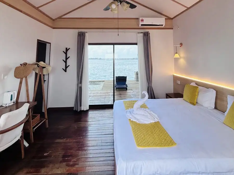 A charming bedroom at Sea Coral Resort near Semporna where the bed faces panoramic glass doors opening onto the balcony with seaviews, authentic dark wood floors, and air con.