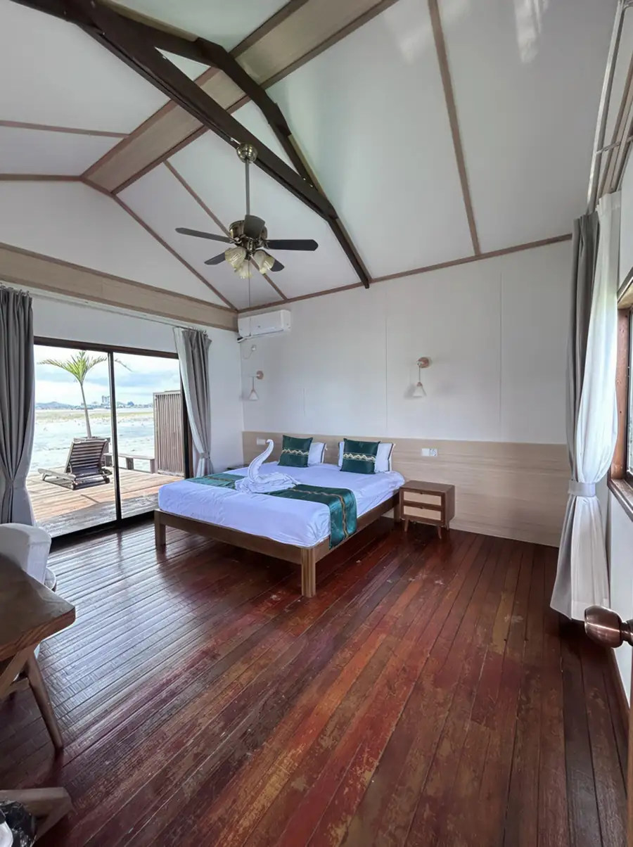 A bright bedroom at Sea Coral Resort in the Celebes Sea where the bed faces panoramic glass doors opening onto the balcony with seaviews, finished with rustic hardwood floors and air con.