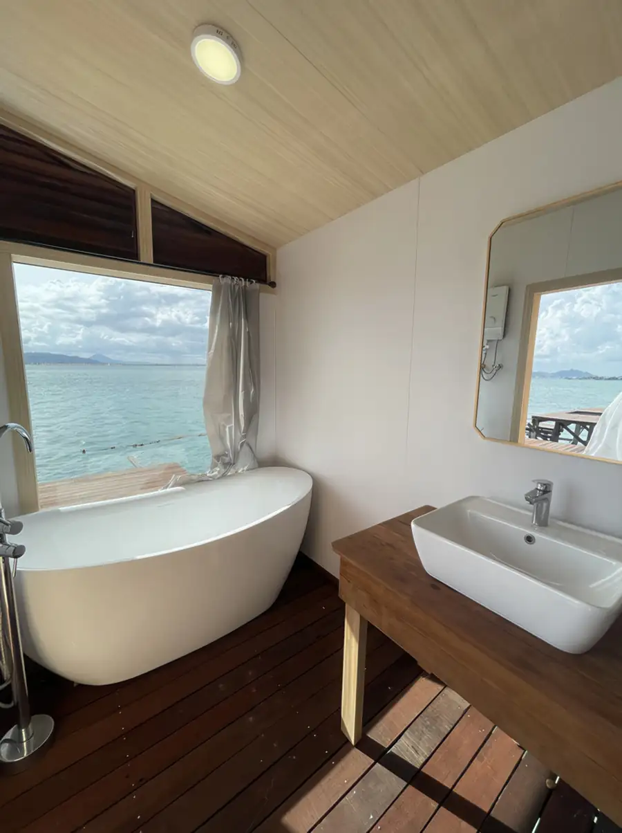 A modern bathroom at Sea Coral Resort featuring a freestanding white bathtub positioned for ocean views and a minimalist wooden vanity with a ceramic sink.