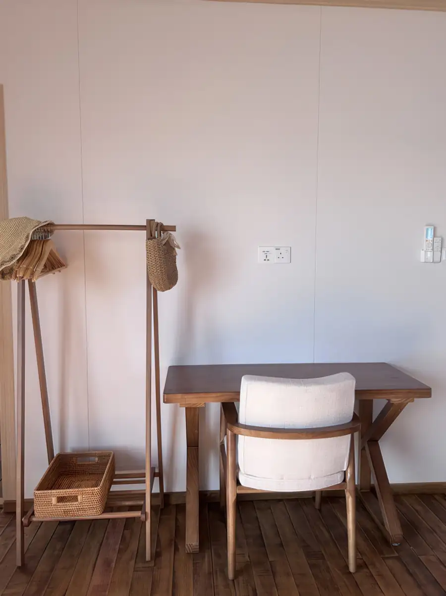 A quiet workspace corner at Sea Coral Resort near the Tun Sakaran Marine Park equipped with a wooden desk, modern chair, rustic clothing rack, rich dark wood floors, and air con.
