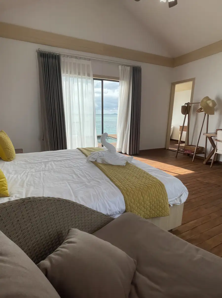 A serene bedroom at Sea Coral Resort in the Celebes Sea with a large bed facing glass doors opening onto the private balcony, authentic glossy hardwood floors, and A/C.