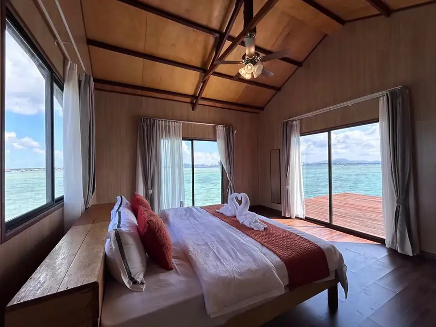 A spectacular waterfront room at Sea Coral Resort in the Celebes Sea showing a bed facing panoramic glass doors opening onto the balcony with seaviews, elegant wood floors, and AC.