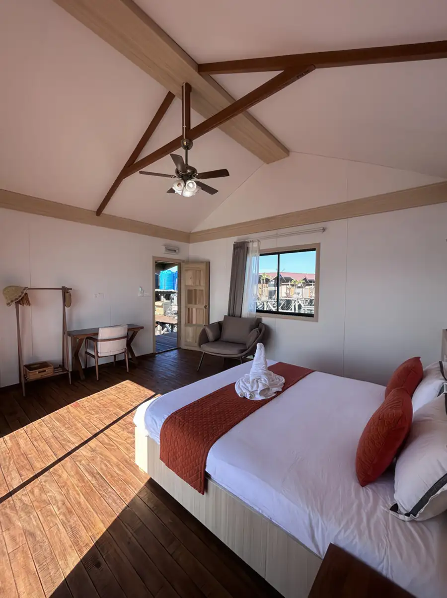 A bright bedroom at Sea Coral Resort near the Tun Sakaran Marine Park highlighting a large bed, seating area, rustic timber floor with smooth wooden boards, ceiling fan, and AC.