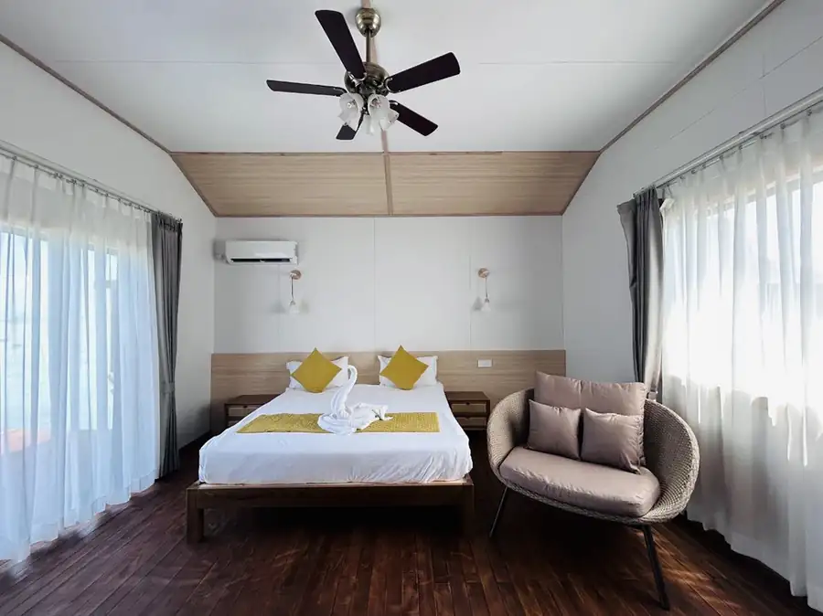 A comfortable suite at Sea Coral Resort near Semporna presenting a large bed, modern seating, floor to ceiling glass doors for private balcony access, elegant hardwood floors, and a/c.