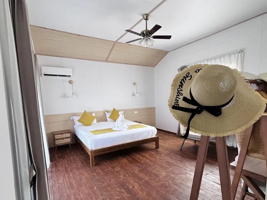 A welcoming room at Sea Coral Resort near the Tun Sakaran Marine Park displaying a cozy bed, stylish hat rack, vaulted ceilings, beautifully polished teak wood floors, and air conditioning.