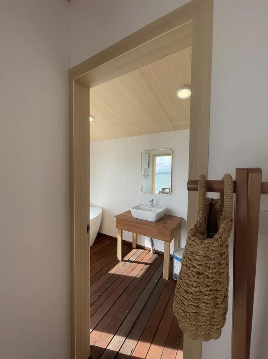 A practical vanity area at Sea Coral Resort near Semporna featuring a modern washbasin, mirror with ocean views, rustic slatted wooden floors, and aircon.